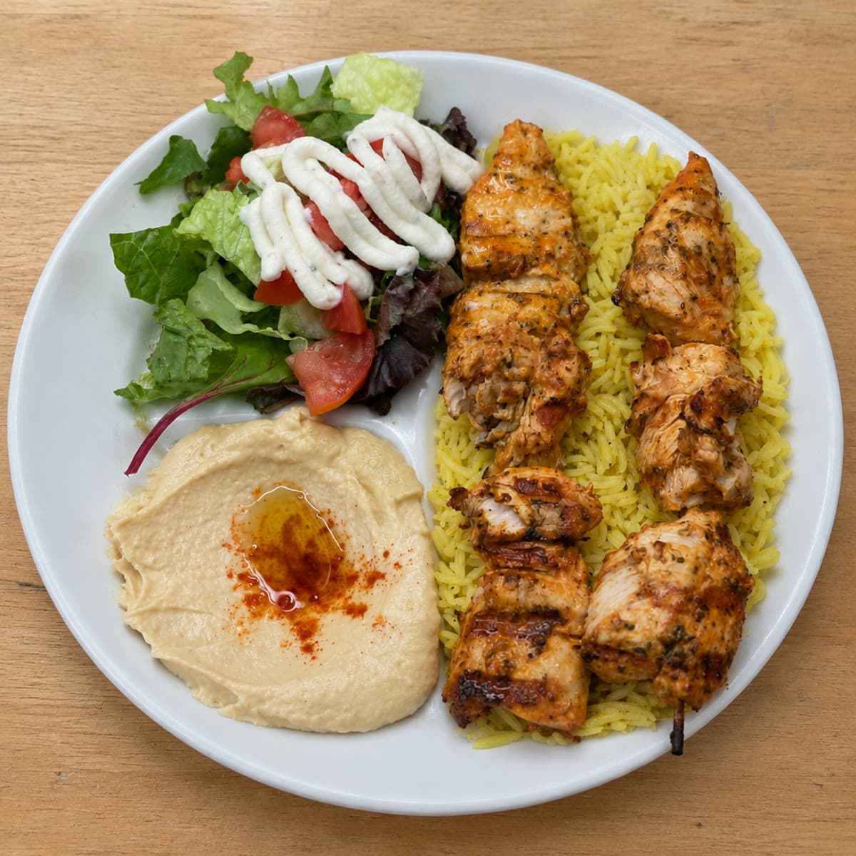 A Mediterranean platter — grilled protein over yellow rice with hummus, salad, garlic sauce and warm pita